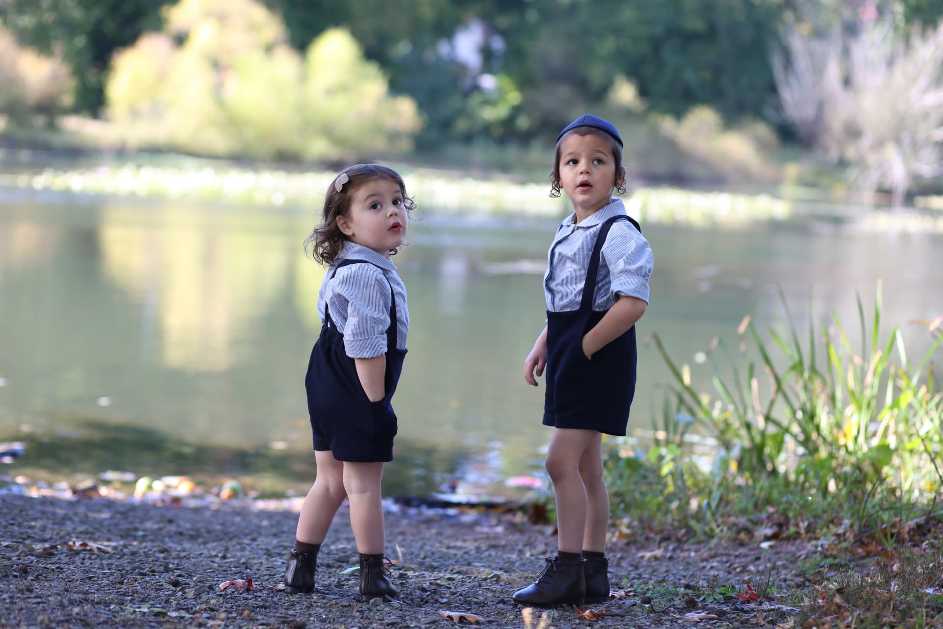A little sister and big brother in matching suspenders, both looking up at something overhead.
