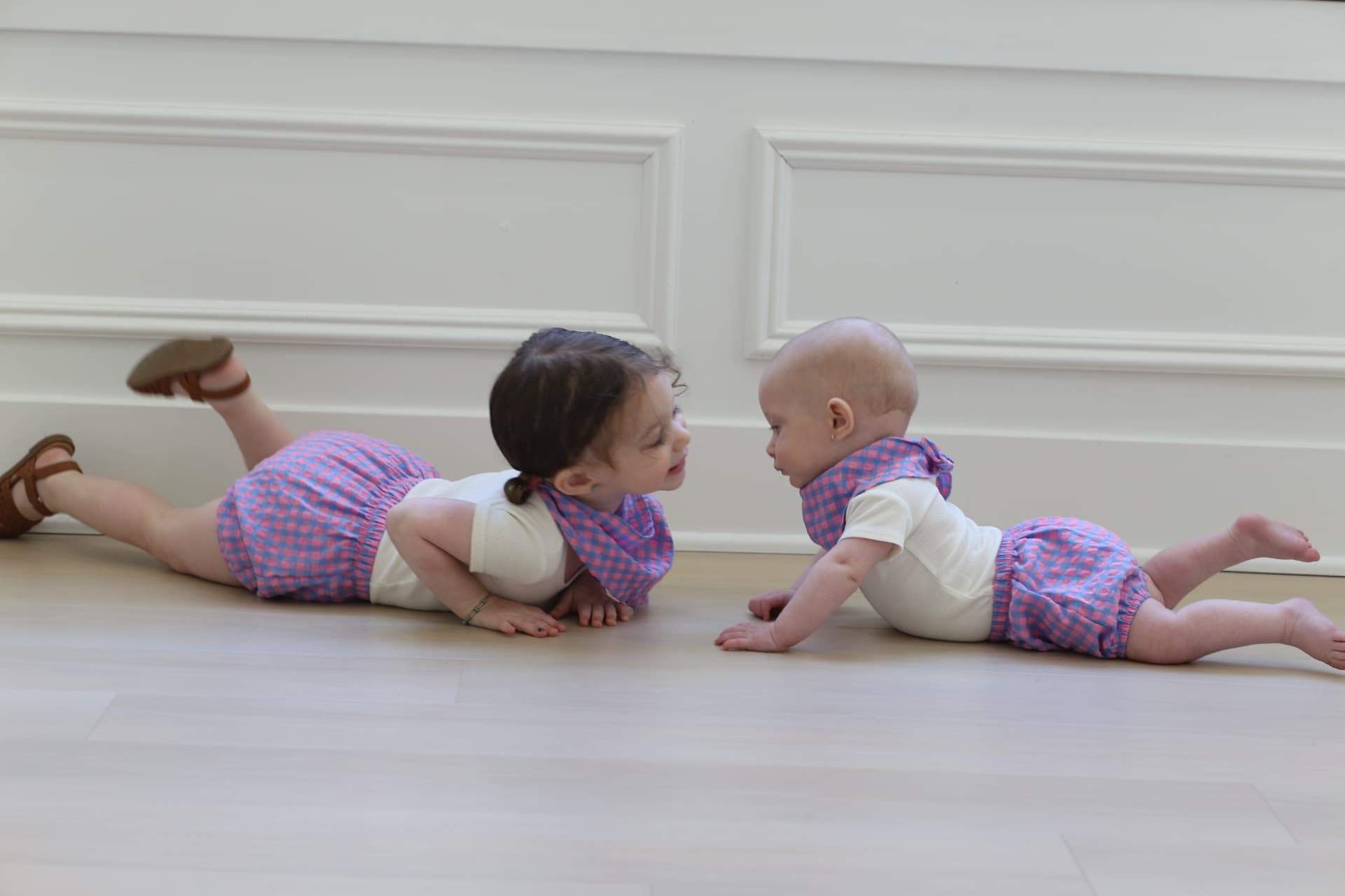 Sister and baby face to face on the floor.