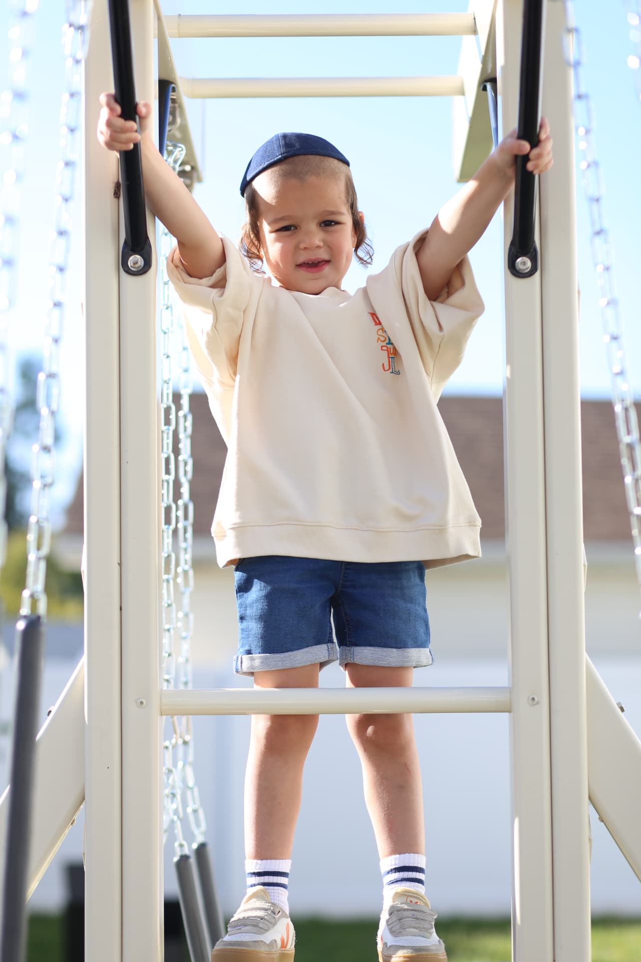 A boy gripping the bars of the playset, both arms stretched wide.