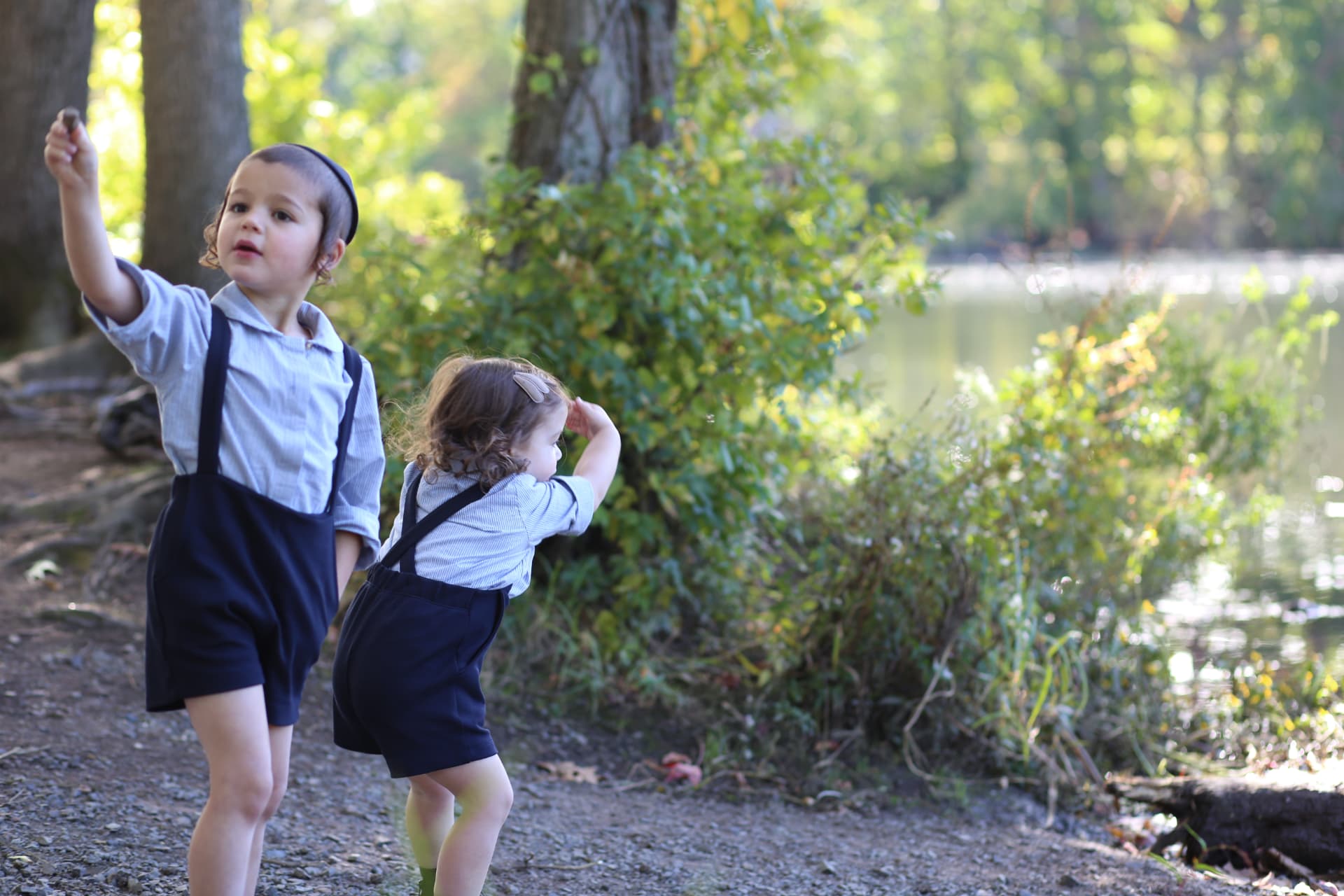 A boy holding a pebble high while his little sister winds up beside him.