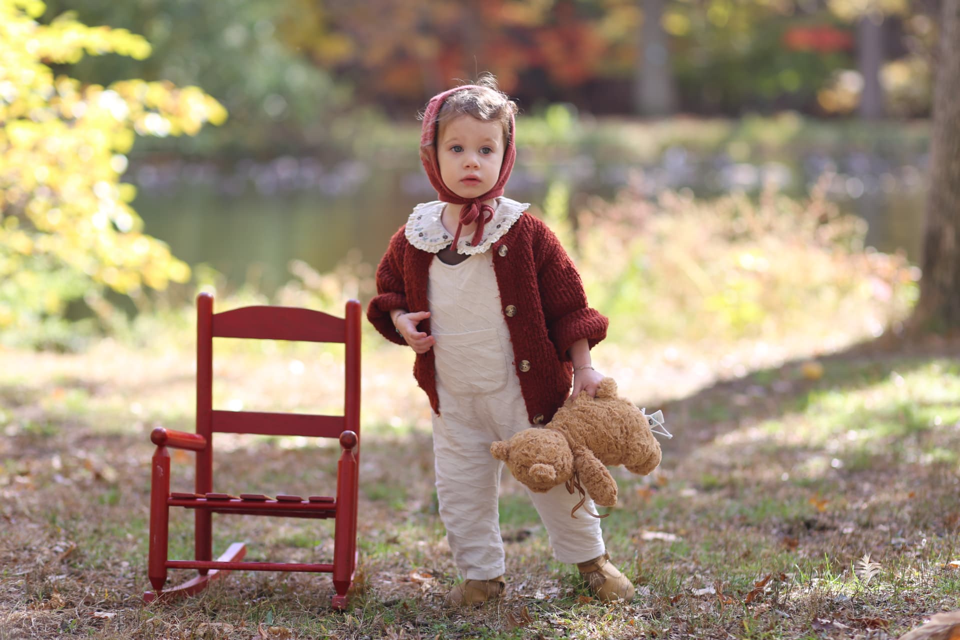 Standing beside the little red chair with her bear.