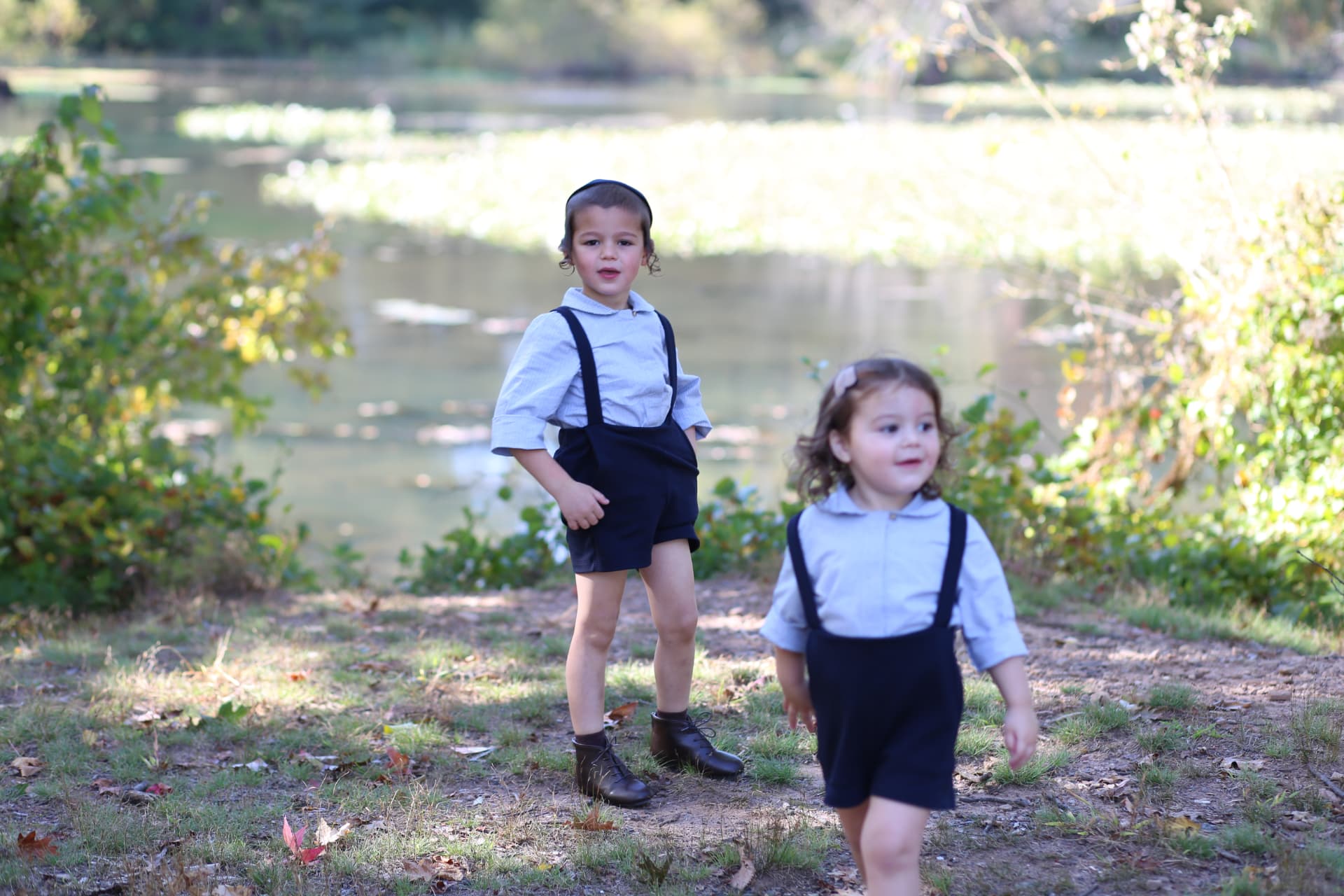 A toddler toddling ahead while her big brother hangs back.