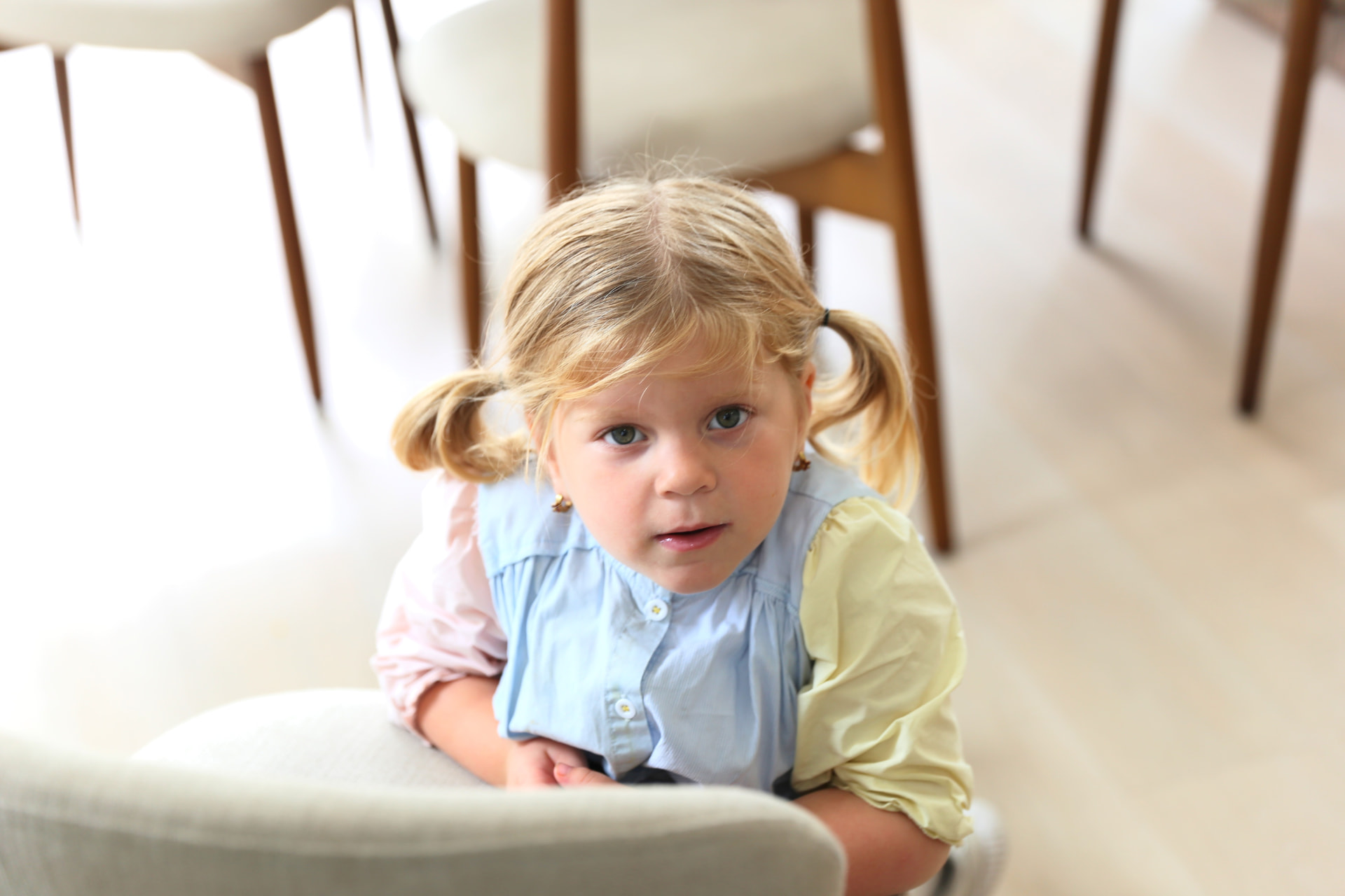 Peeking over a dining chair in pigtails.