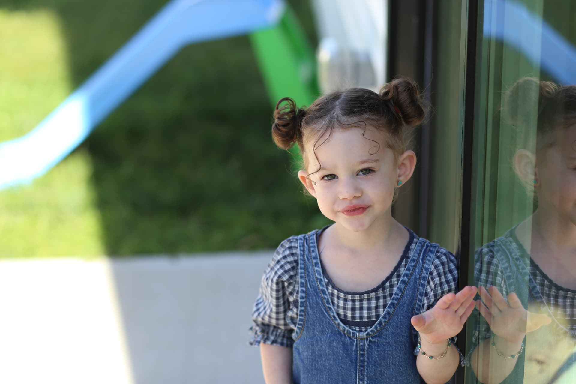 A girl in overalls pressing her hand to the glass.