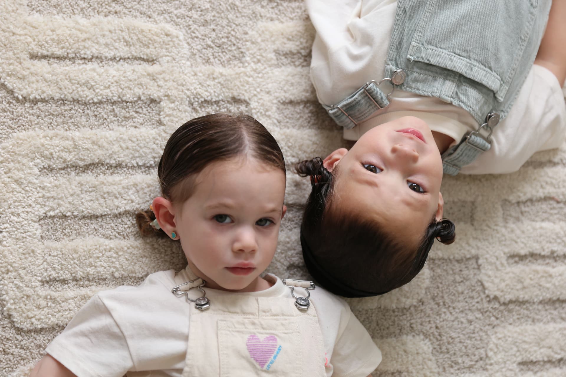 Two sisters lying head to head on the rug.
