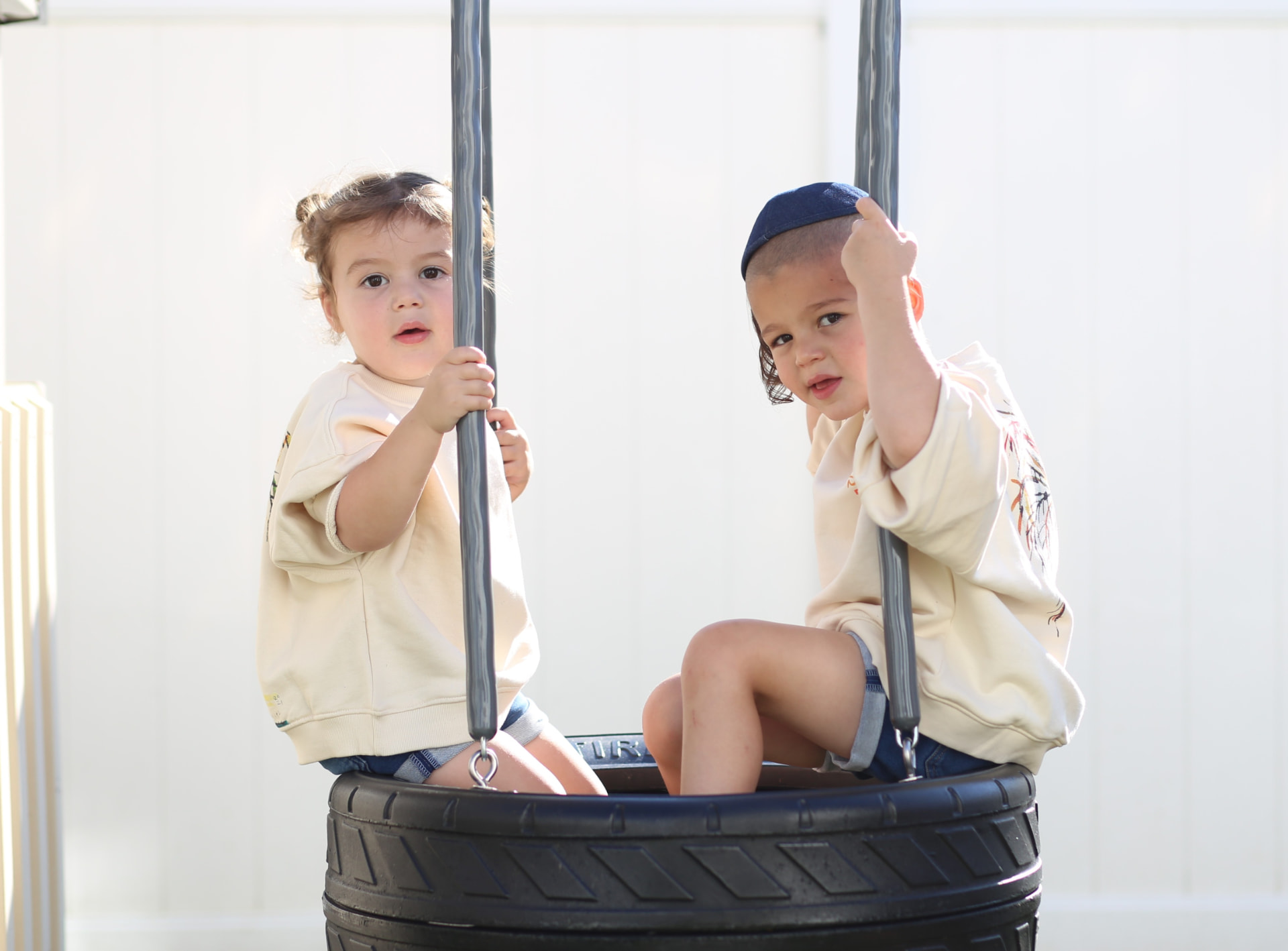 Two kids in matching sweatshirts sharing the tire swing.