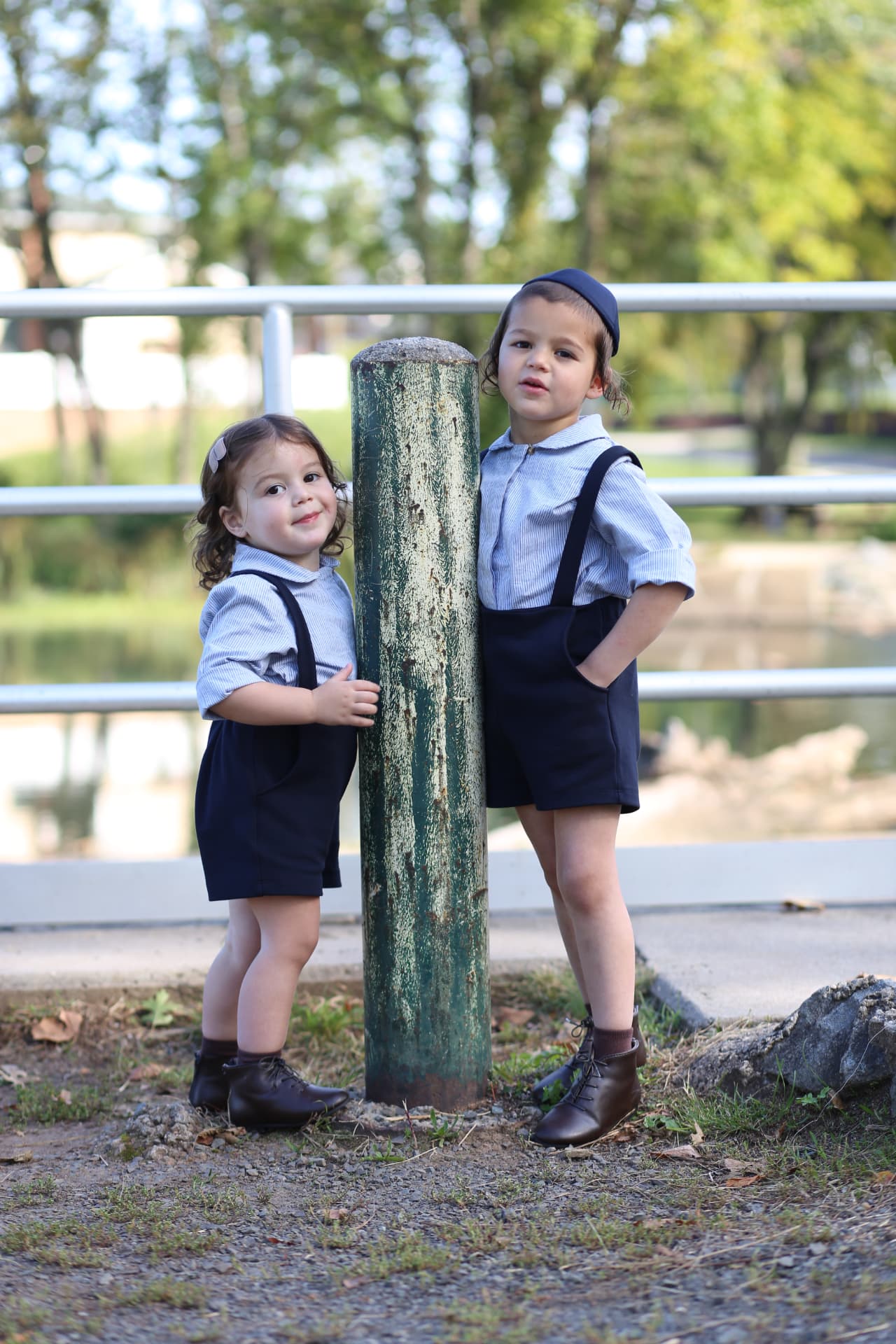 A little sister and her big brother leaning on either side of the old green post.
