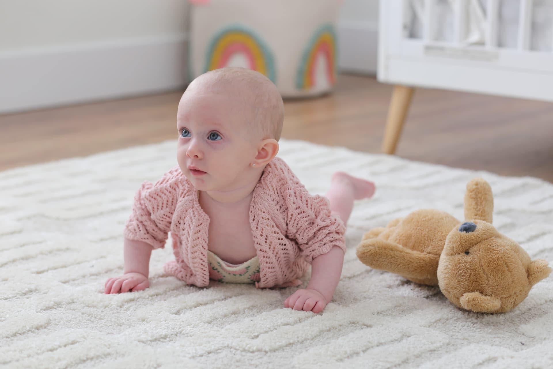 A baby in pink knit on the nursery rug.