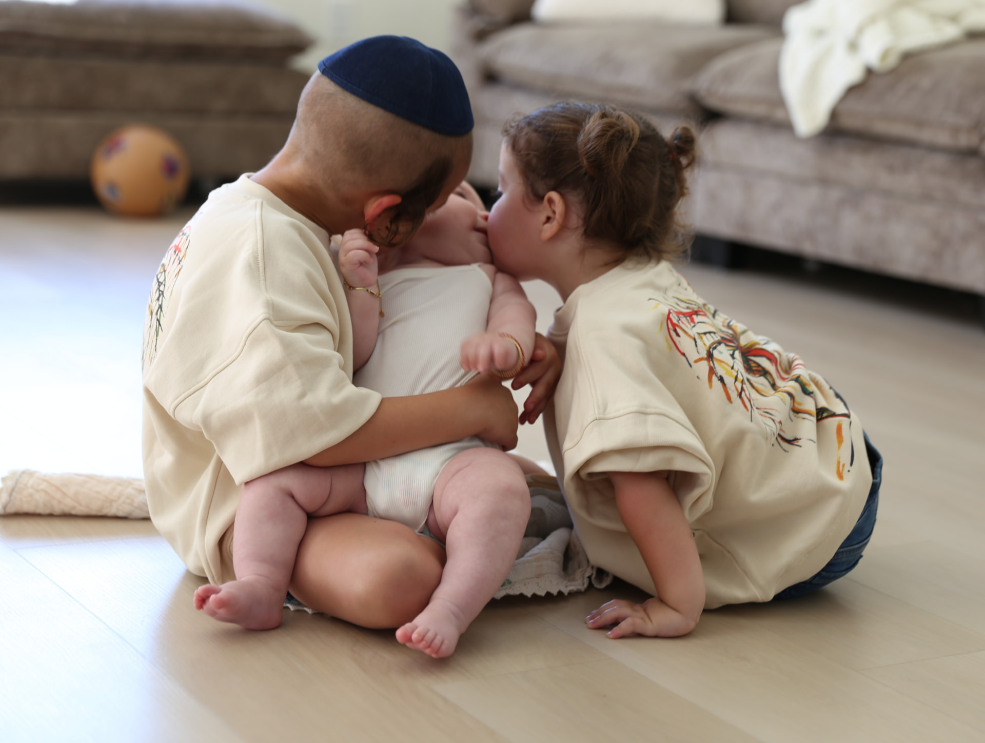 Brother and sister kissing the baby on the living room floor.