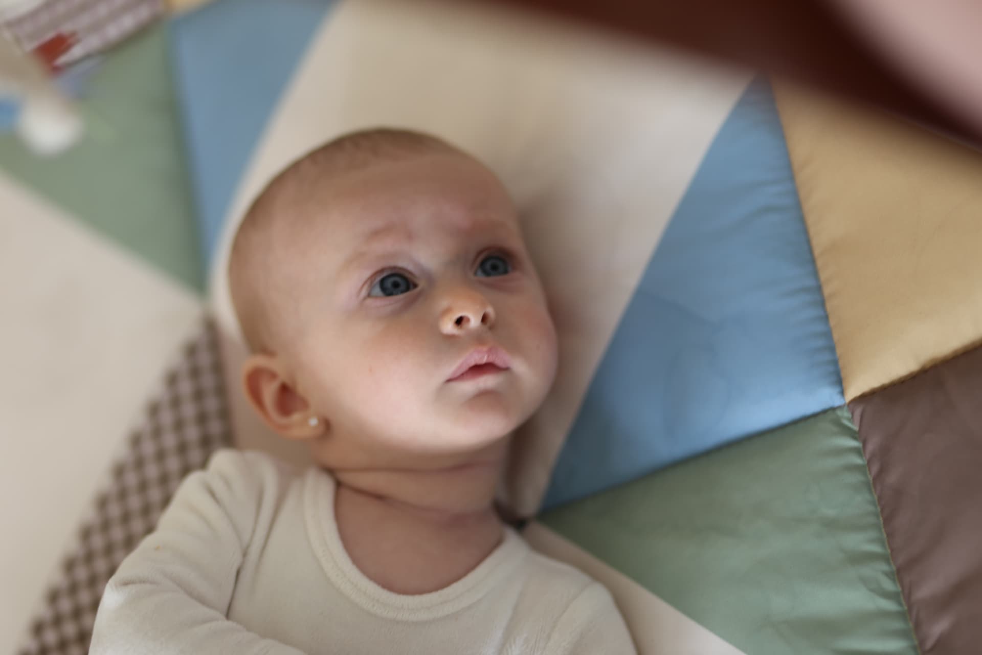 A baby on the patchwork play mat, looking up.