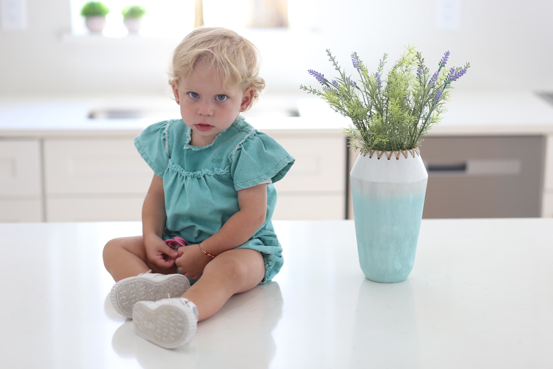 A toddler sitting on the kitchen counter beside the lavender.