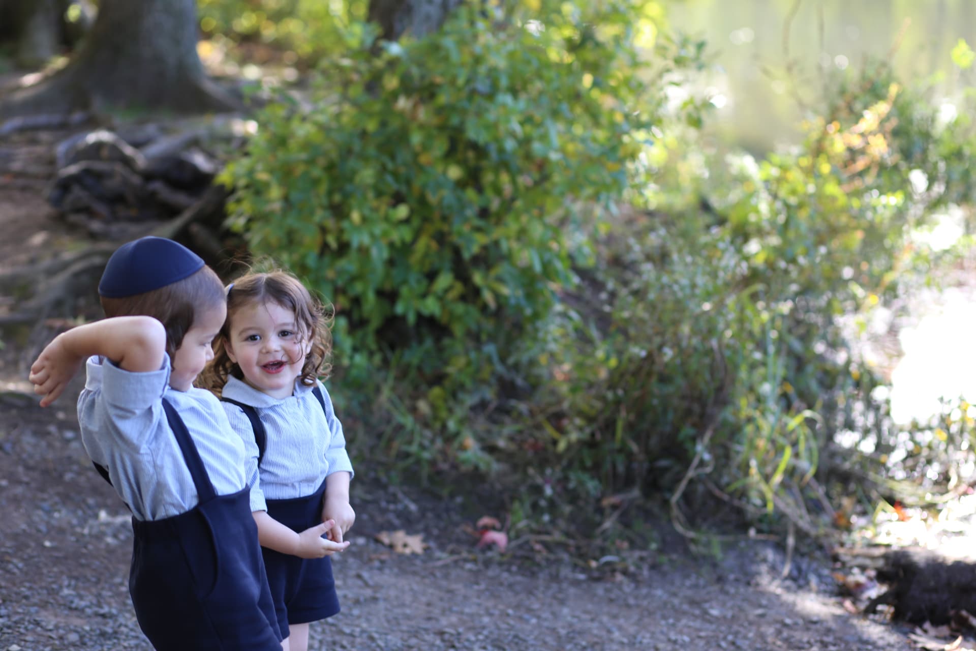A little girl in suspenders grinning beside her brother on the path.