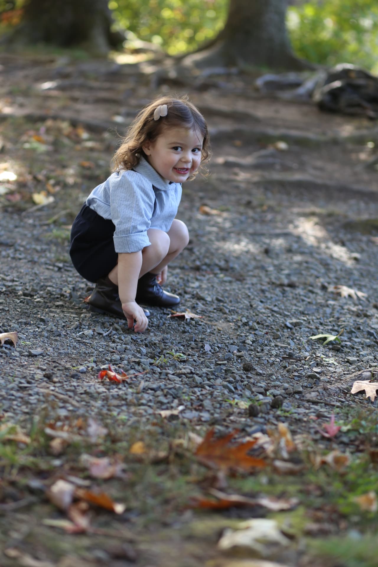 A little girl crouching on the gravel path, smiling back over her shoulder.