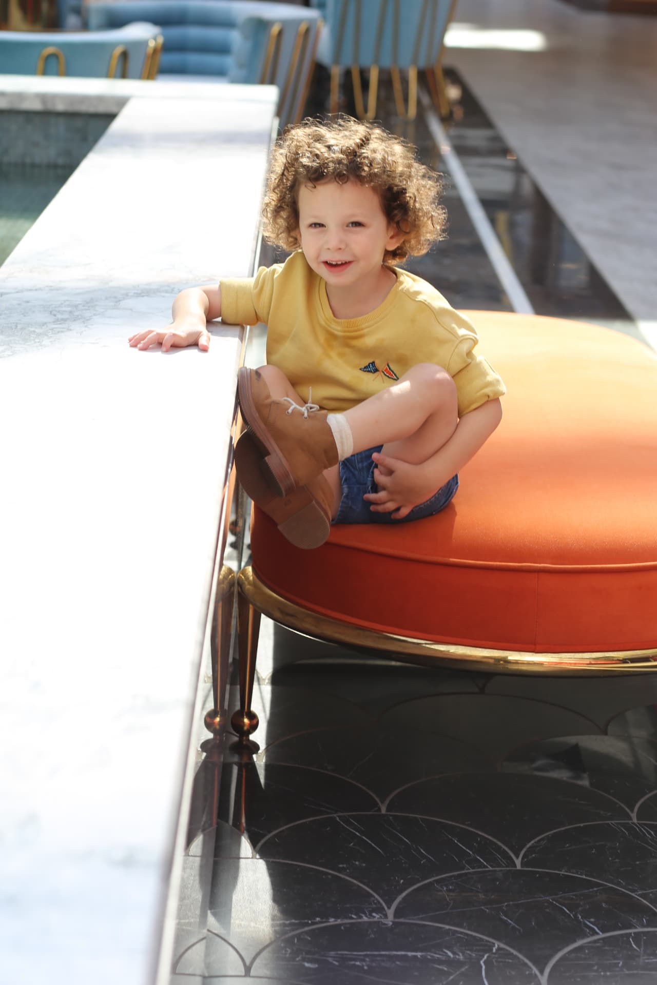 Curls and a yellow shirt on a bright orange seat.