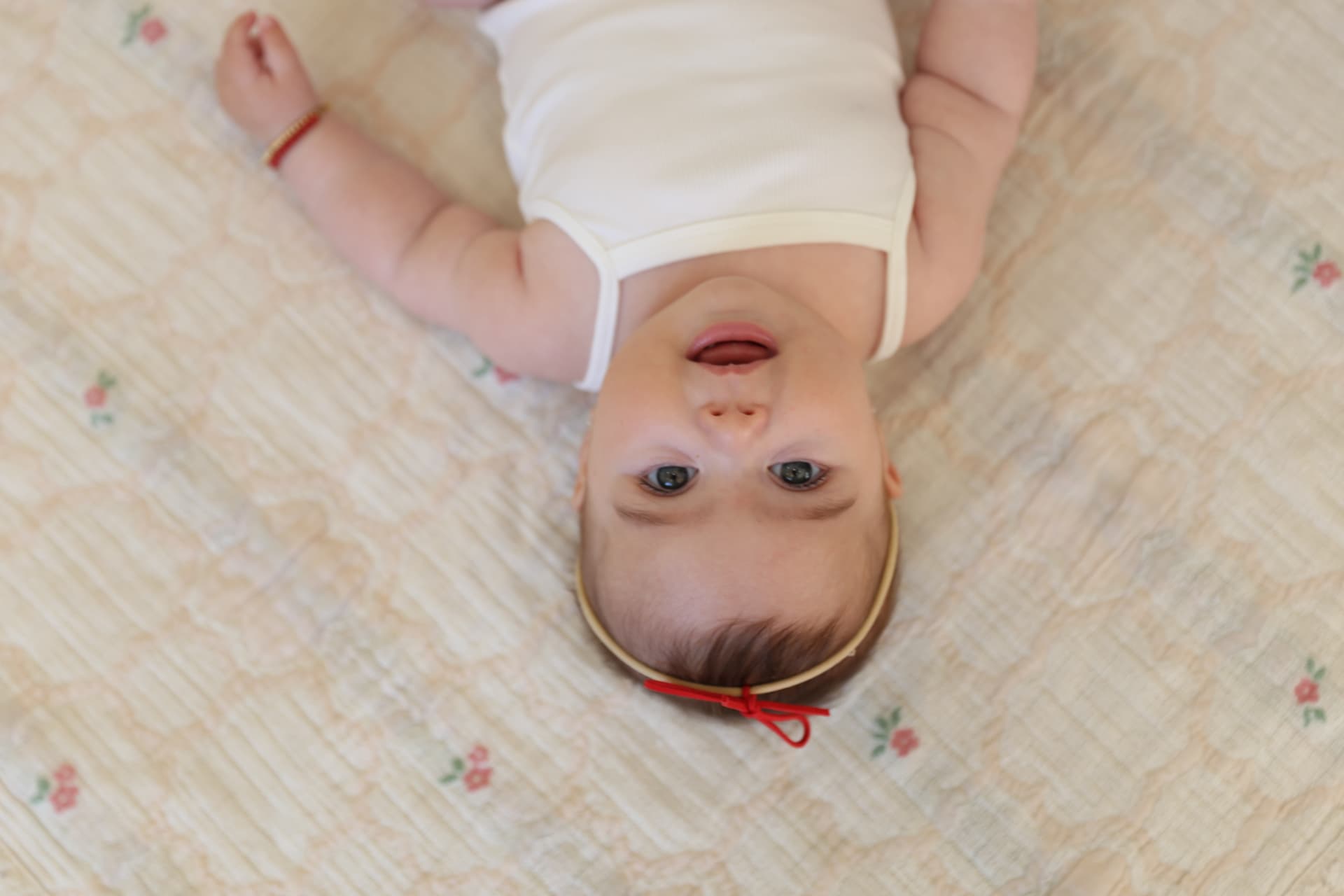 A baby with a red headband bow smiling up from a floral quilt.