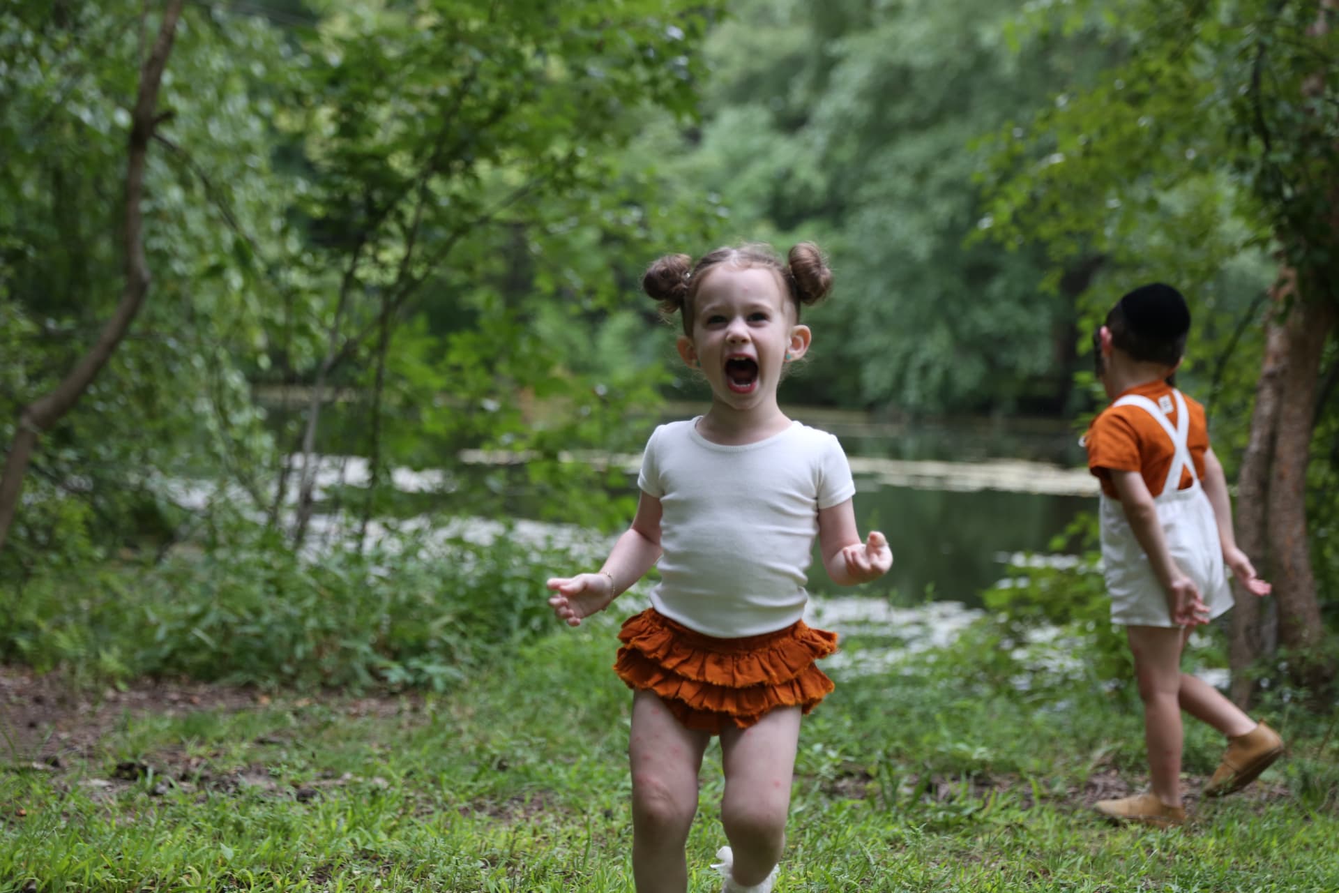 A joyful girl running through the grass by the water.