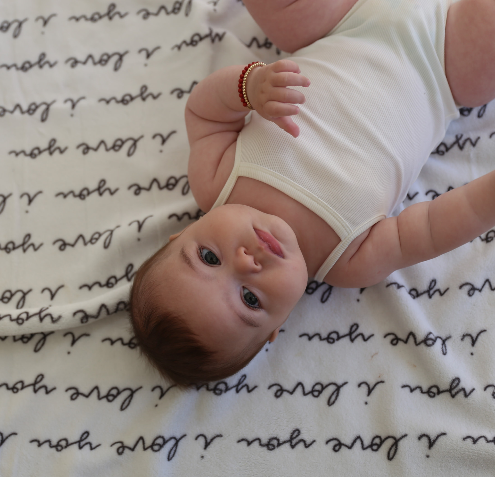 A baby with a beaded bracelet lying on an I love you blanket.