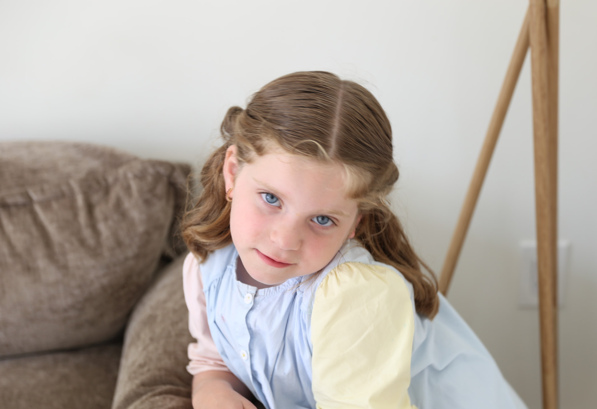 A girl in a pastel dress leaning on the couch.