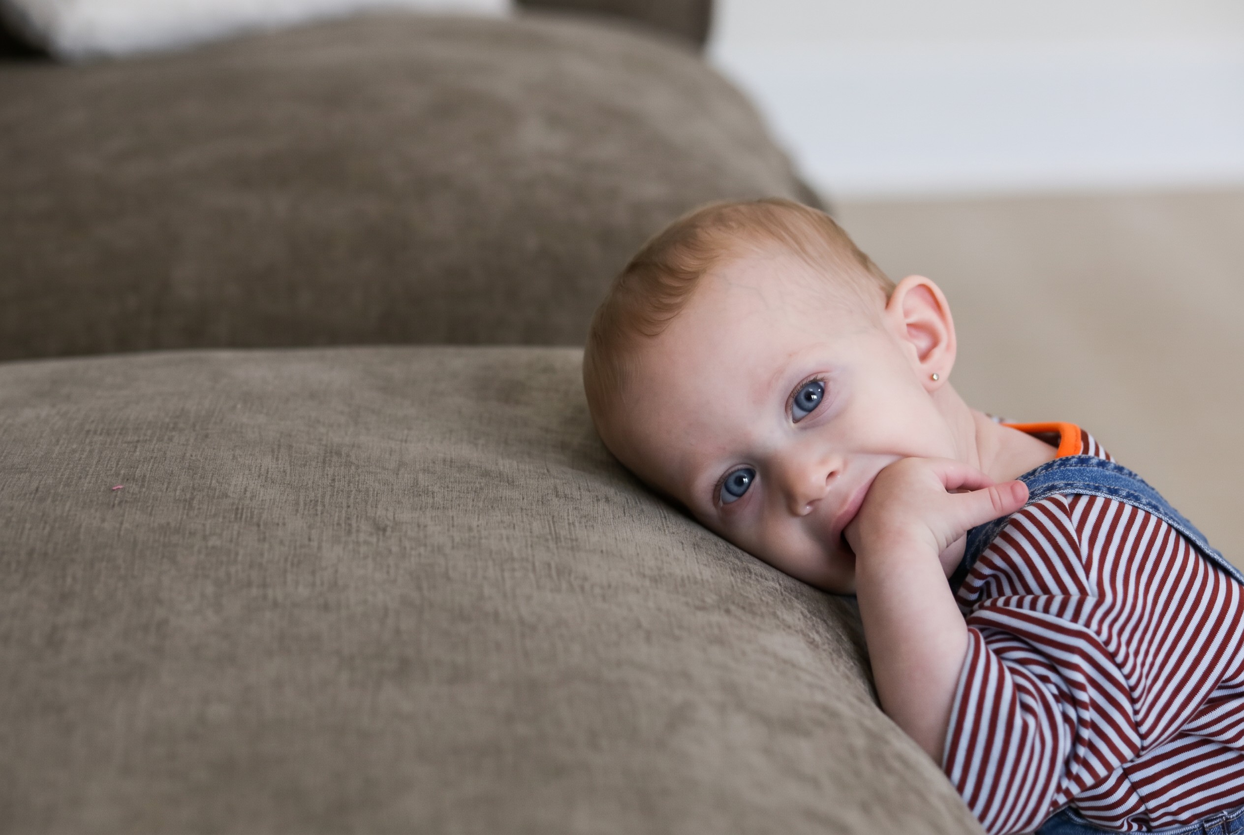 A baby leaning on the couch, fingers in her mouth.
