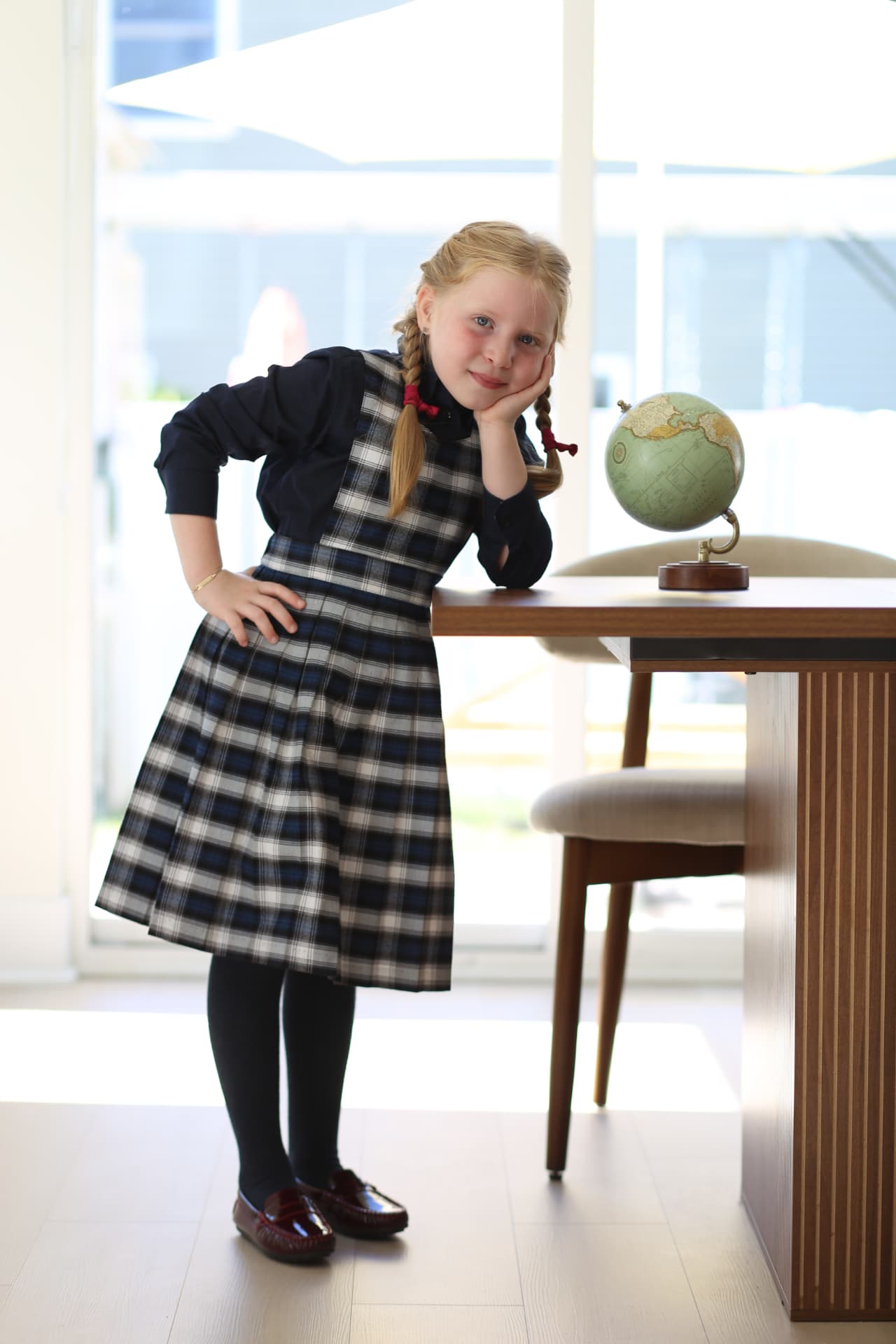 A girl in a plaid jumper leaning on the dining table beside a globe.