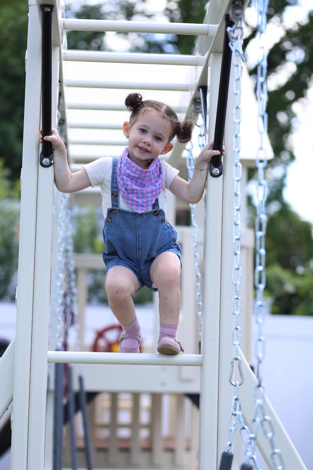 A toddler in denim overalls on a ladder.