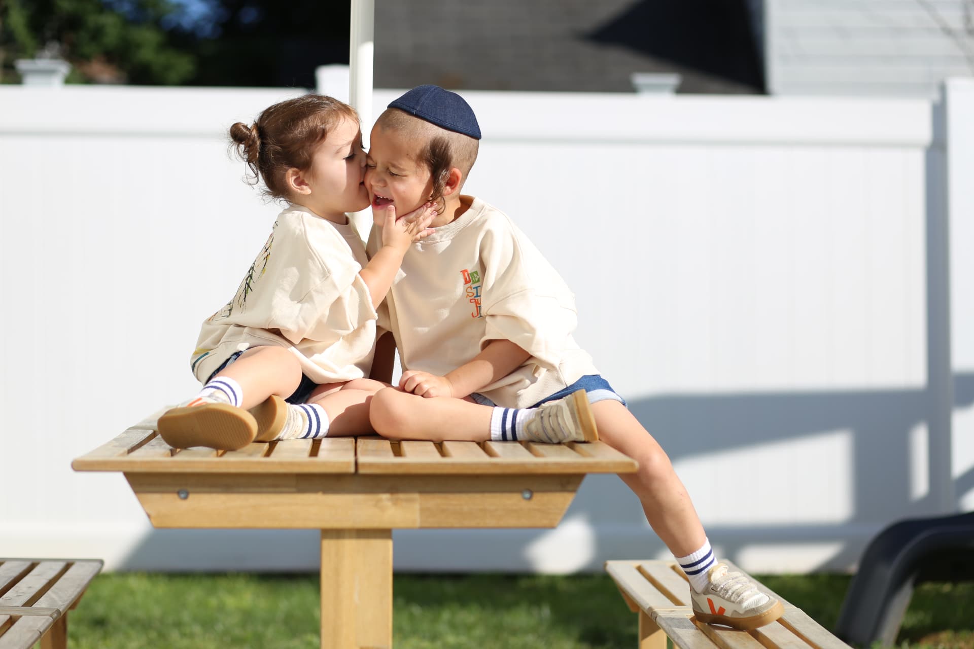 Brother and sister whispering on the backyard picnic table.