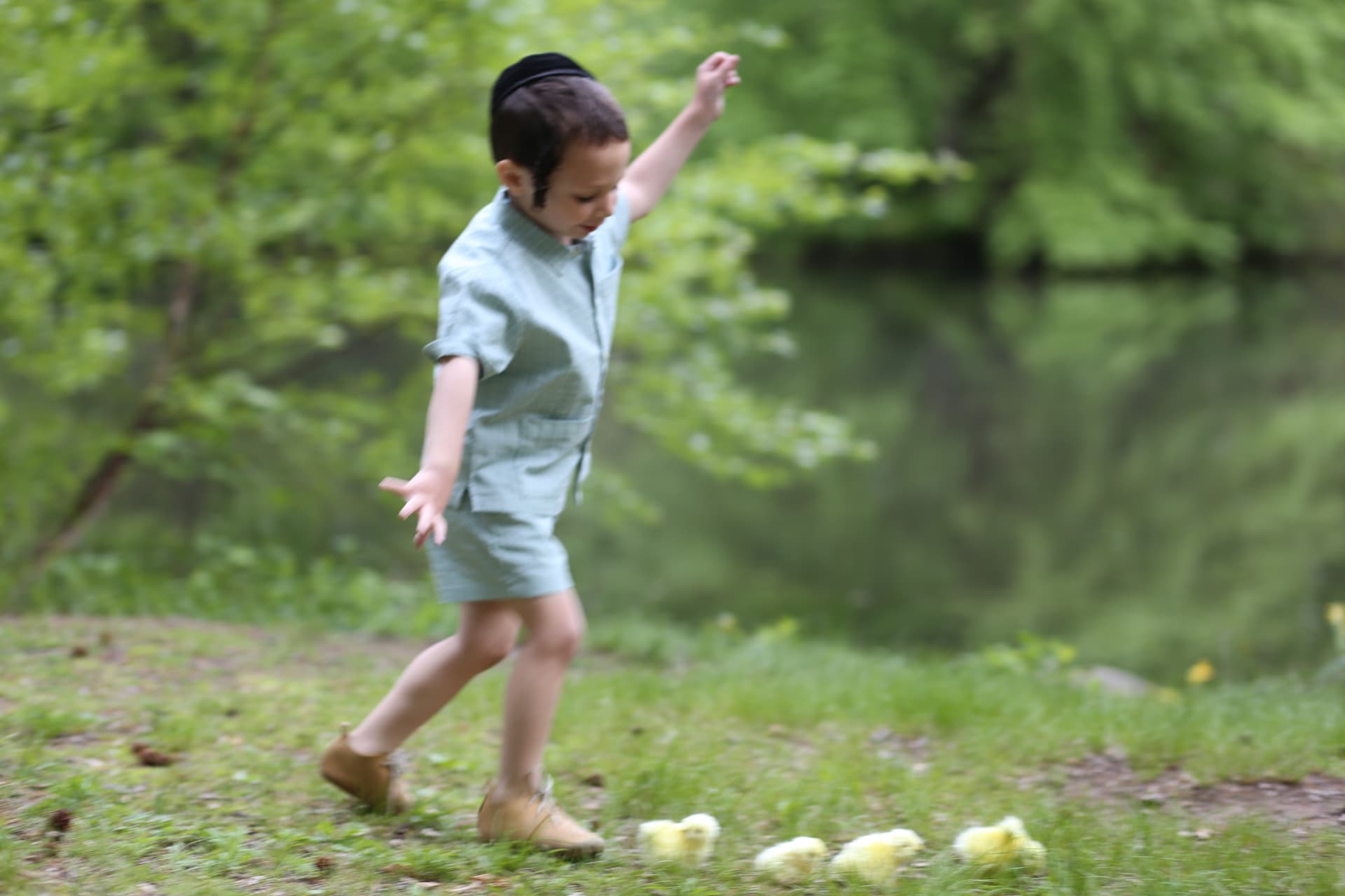 A boy stepping high over a row of baby chicks, arms out for balance.