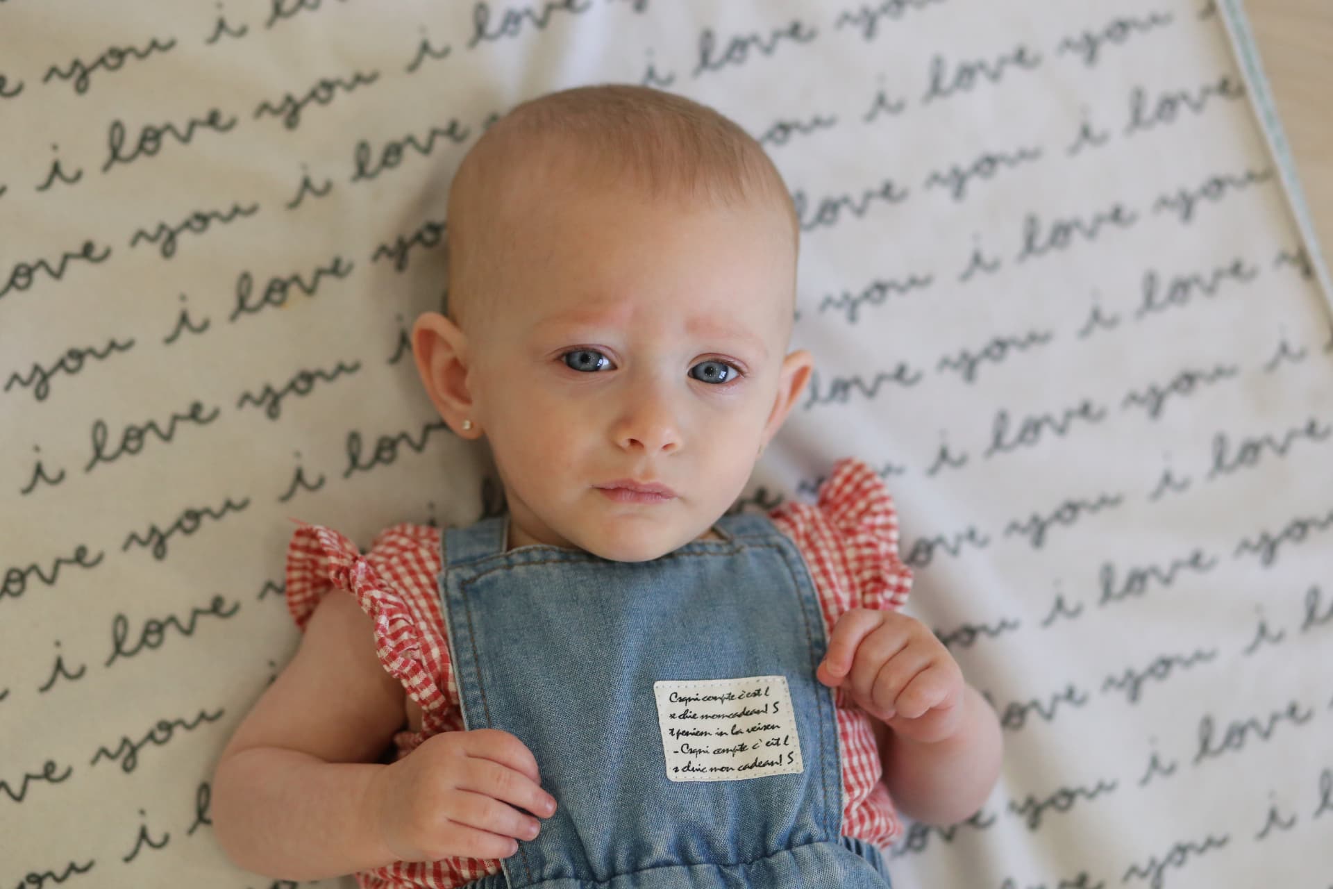 A baby in overalls on a love-note blanket.