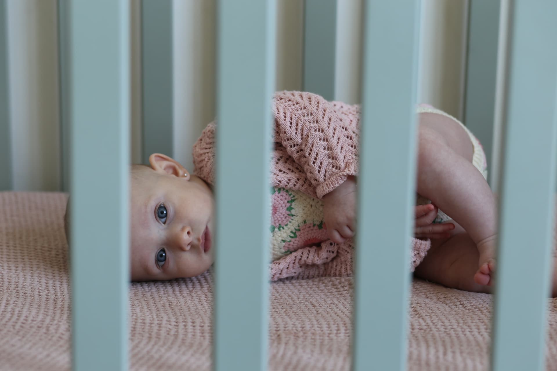 A baby peeking out between the crib bars.
