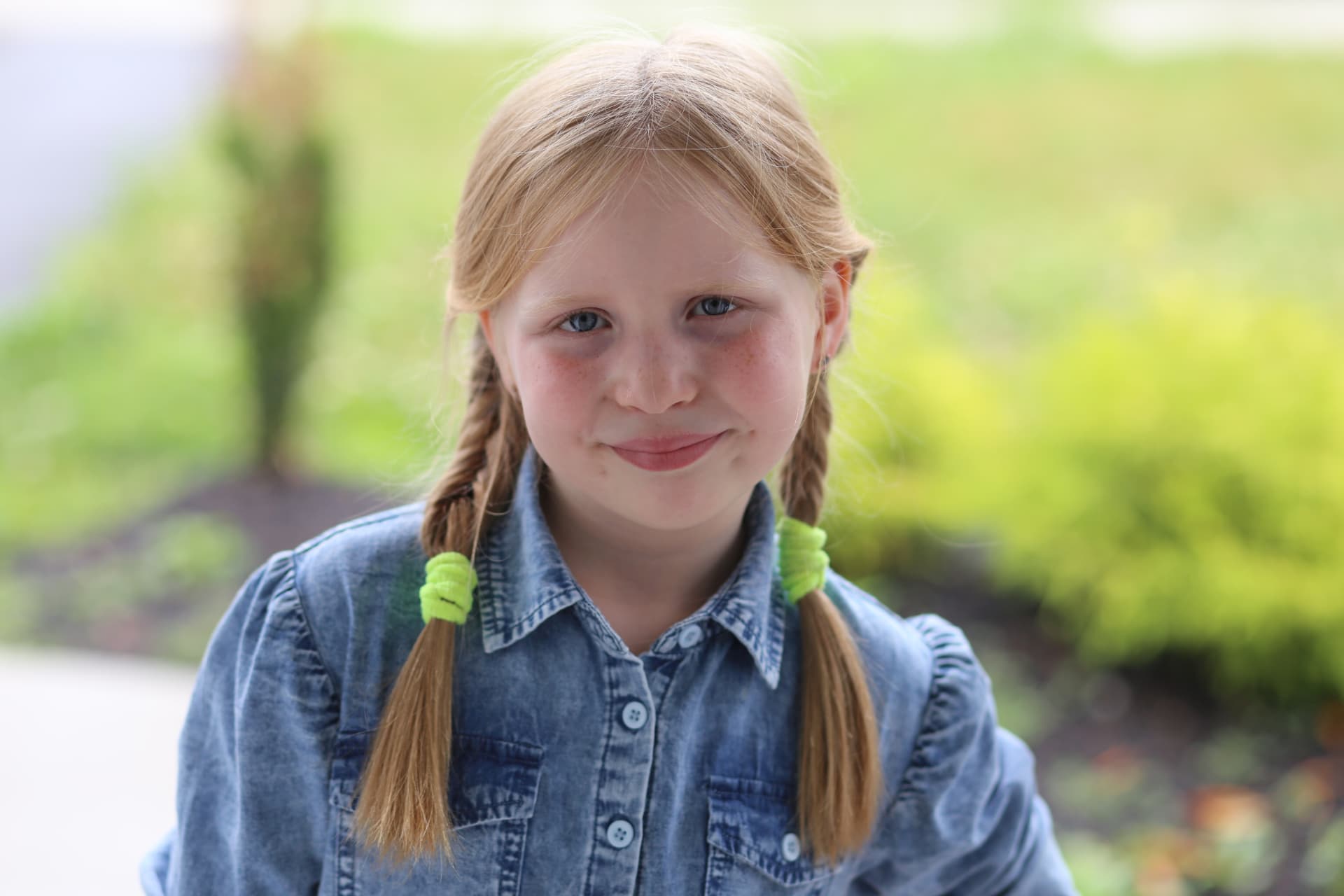 A girl with braids and a denim jacket in the yard.