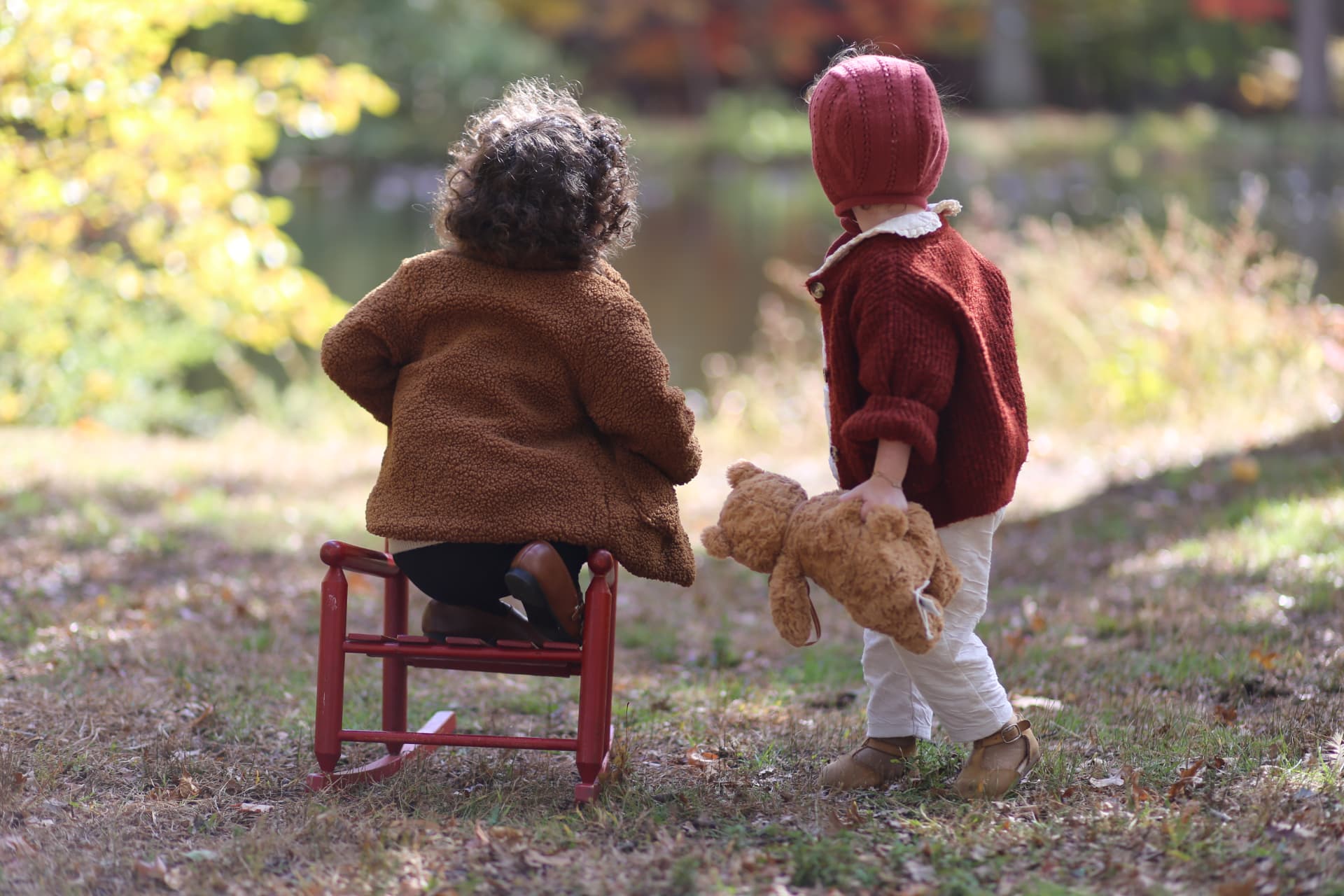 Two little ones and a teddy by the autumn pond.