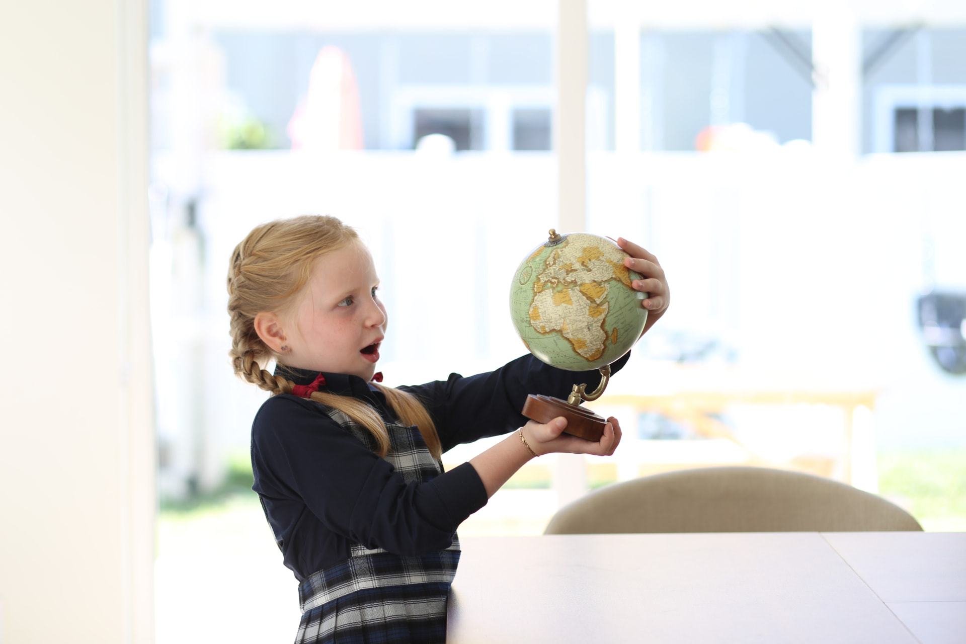 A girl in braids gasping at the globe in her hands by the dining table.