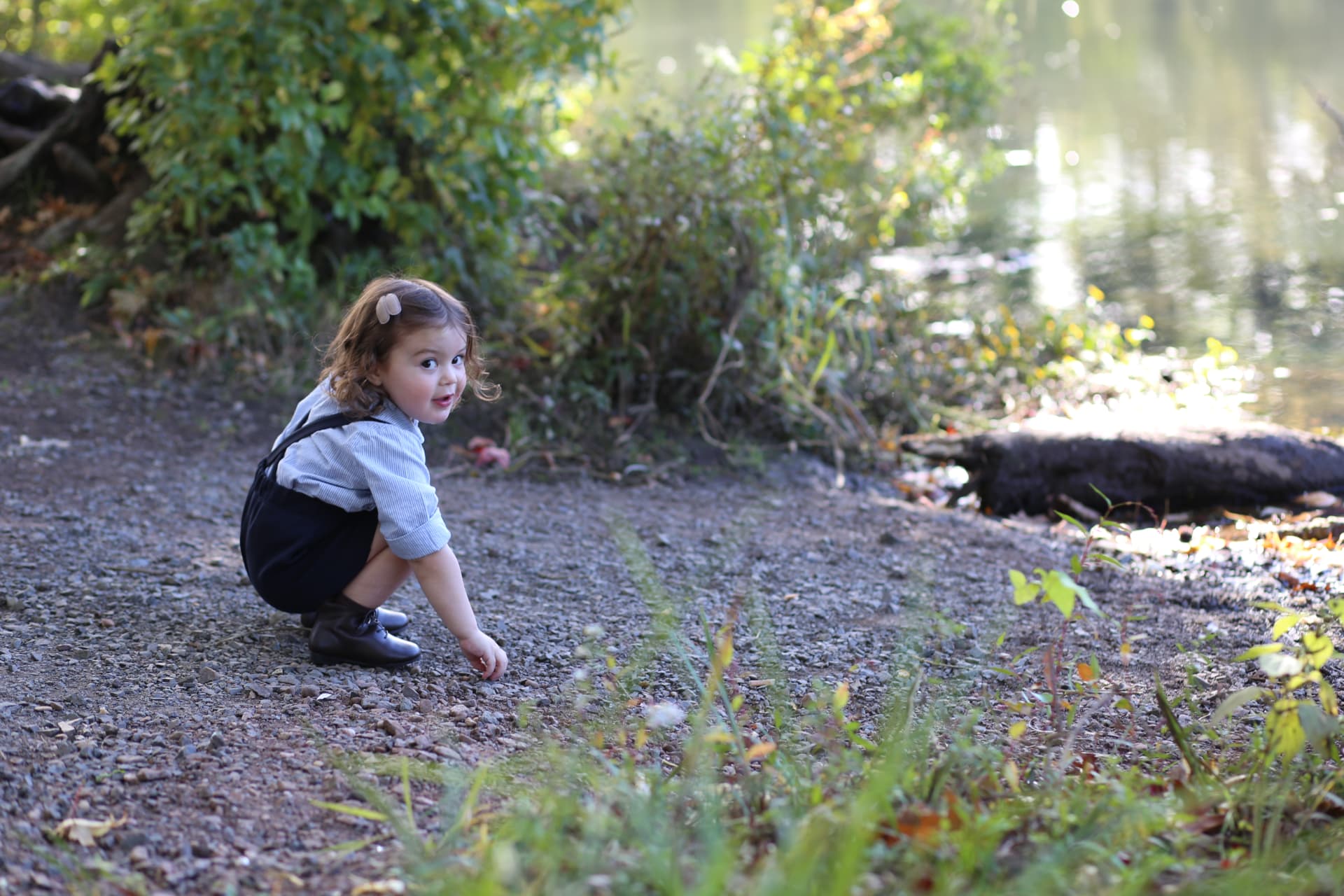 A little girl crouching on the gravel path, looking back over her shoulder.