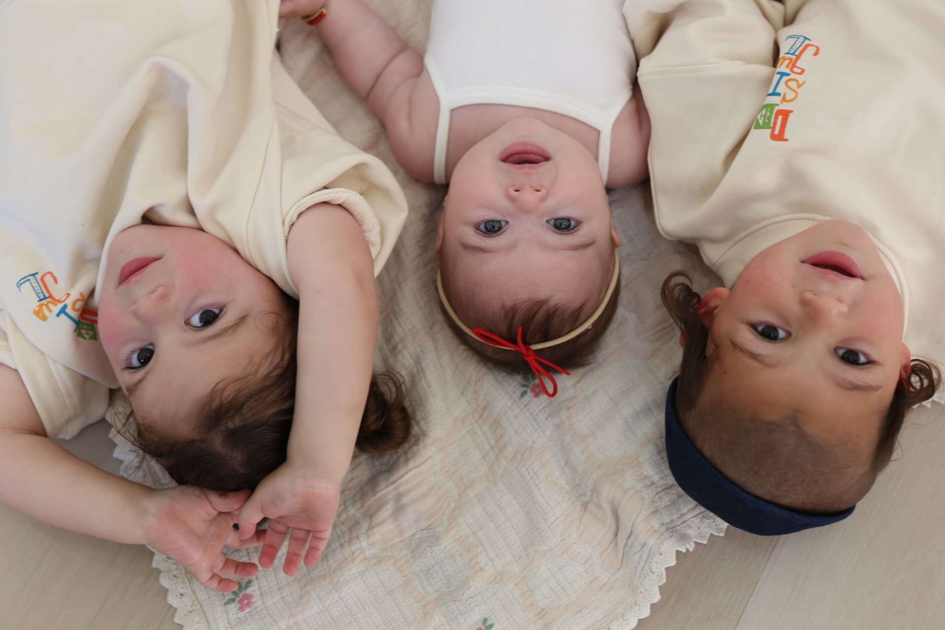 Three siblings lying upside down on a blanket, looking up.